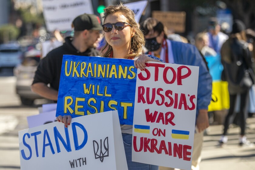 A protester holds signs including "Ukrainians will resist" and "Stop Russia's war on Ukraine."