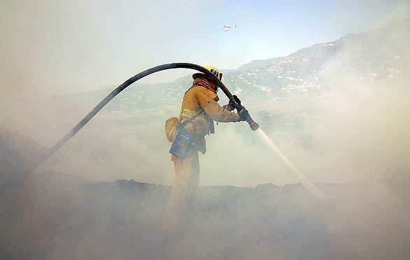 Hampered by intense winds and blowing smoke, an L.A. City firefighter douses flames in the hills above Sylmar.