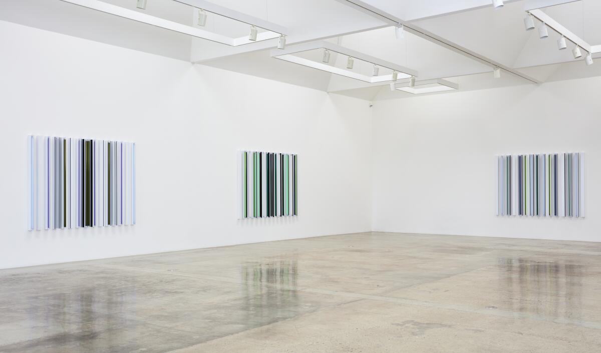 A series of three rectangular geometric pieces  made from fluorescent tubes are visible in a white-walled gallery