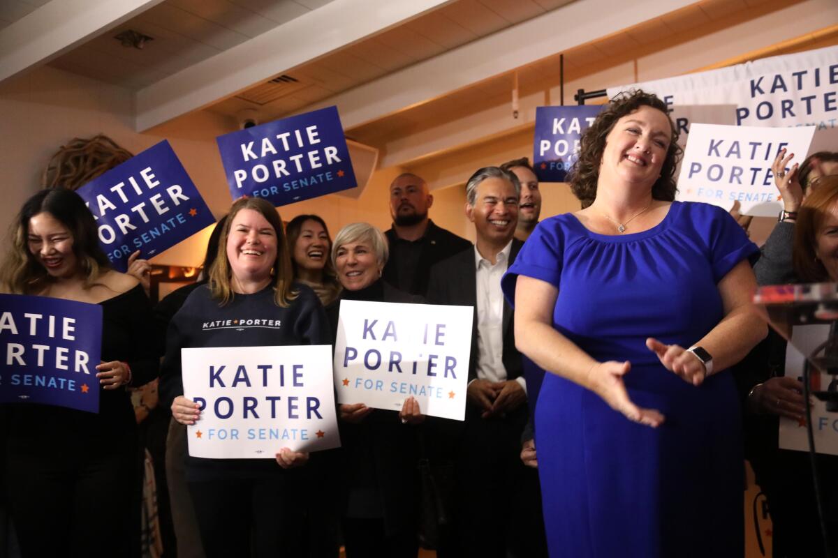 Katie Porter standing with a crowd of supporters holding blue-and-white campaign signs