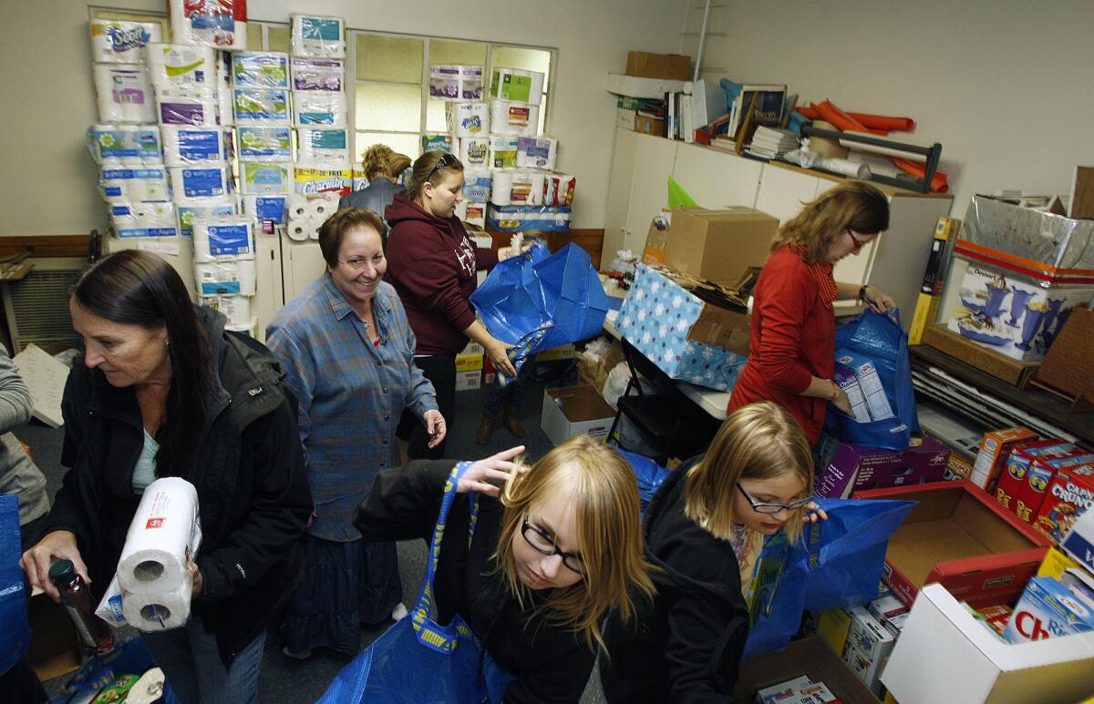 Janet Diel, president of the Burbank Coordinating Council, smiling in the center, moves among a crush of volunteers in a small room stacked nearly to the ceiling with donated grocery items that the volunteers are assembling into Holiday Baskets at the Little White Chapel in Burbank, in this file photo taken on Dec. 11, 2013.