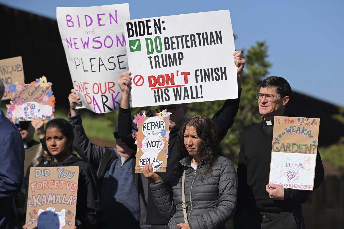 People hold signs reading "Biden: Do Better Than Trump, Don't Finish His Wall!" and others.