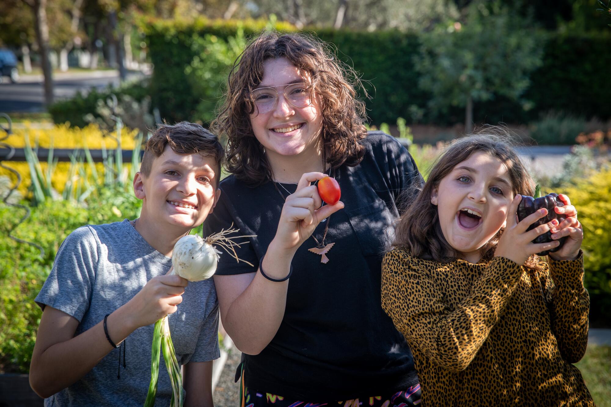The Matloff kids — Daniel, Isabelle and Edie — smile as they show off fresh-picked veggies.