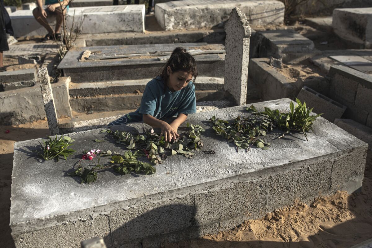 A Palestinian girl lays roses on the grave of one of the children of Nijim family at Al-Faluja cemetery in Jabalia in the northern Gaza Strip, Tuesday, Aug. 16, 2022. A Palestinian human rights group and an Israeli newspaper reported Tuesday that an explosion in a cemetery that killed five Palestinian children during the latest flare-up in Gaza was caused by an Israeli airstrike and not an errant Palestinian rocket. (AP Photo/Fatima Shbair)