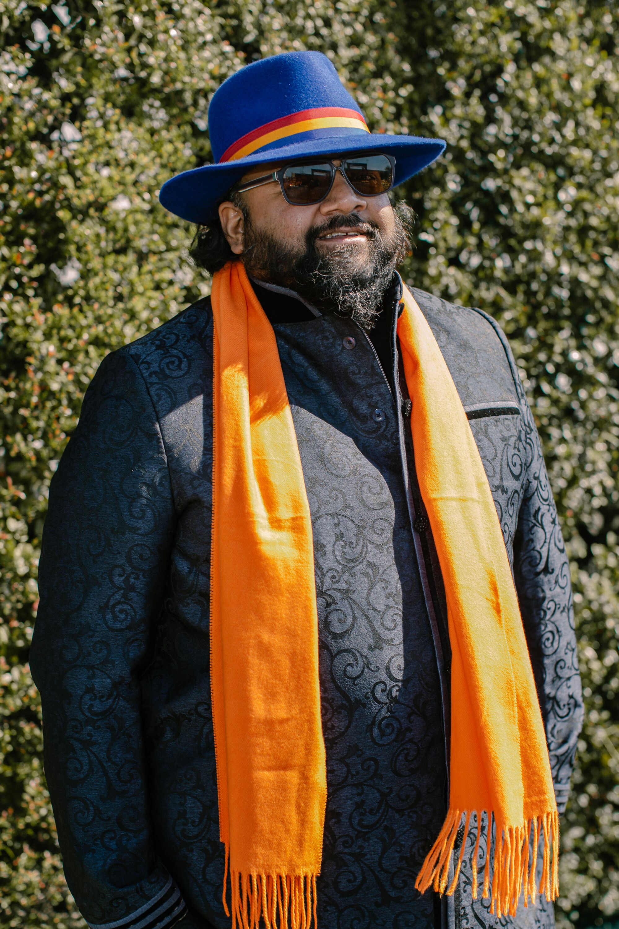 A man in a dark shirt and hat and a bright orange scarf.