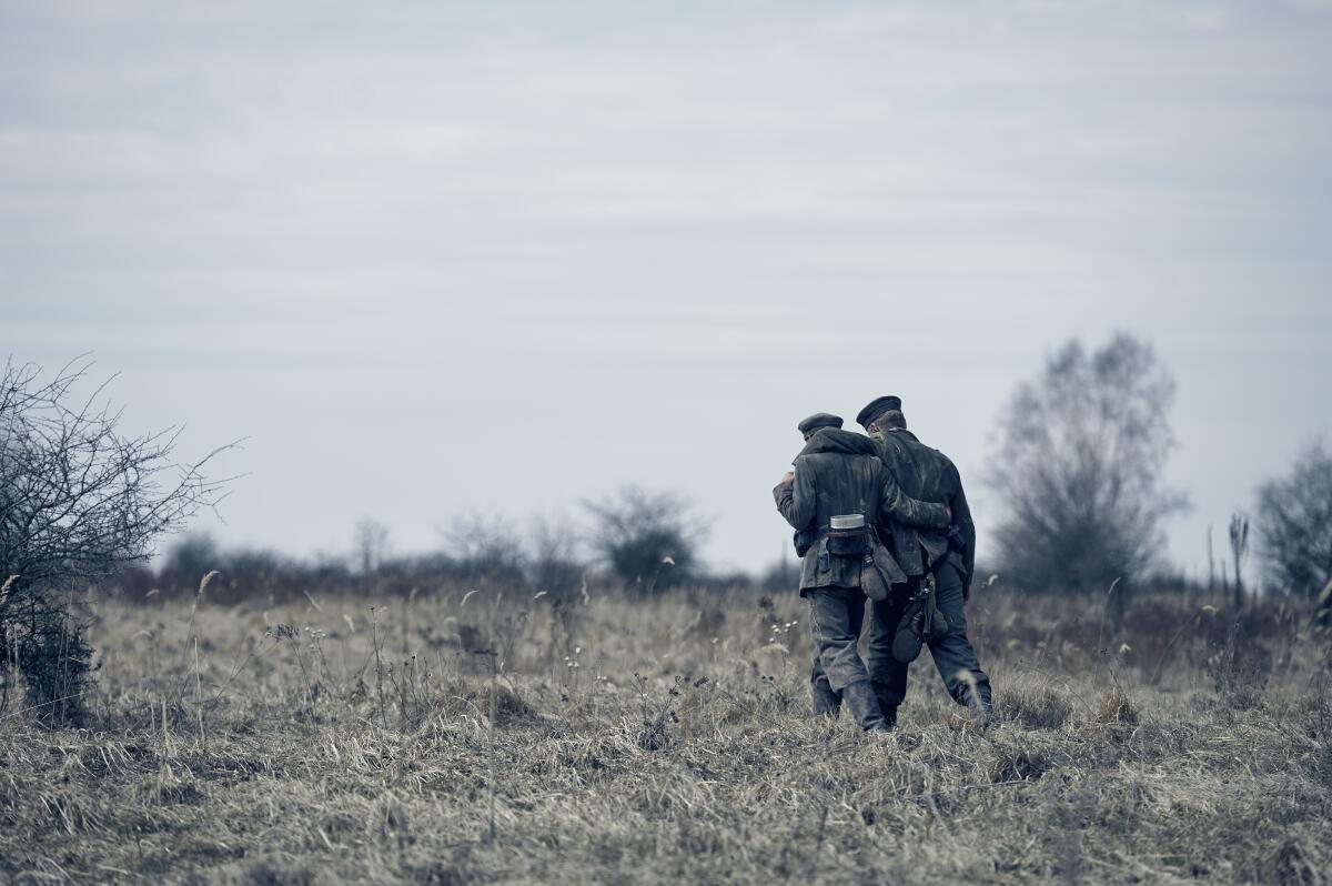 Two soldiers walk in a field on a cloudy day.