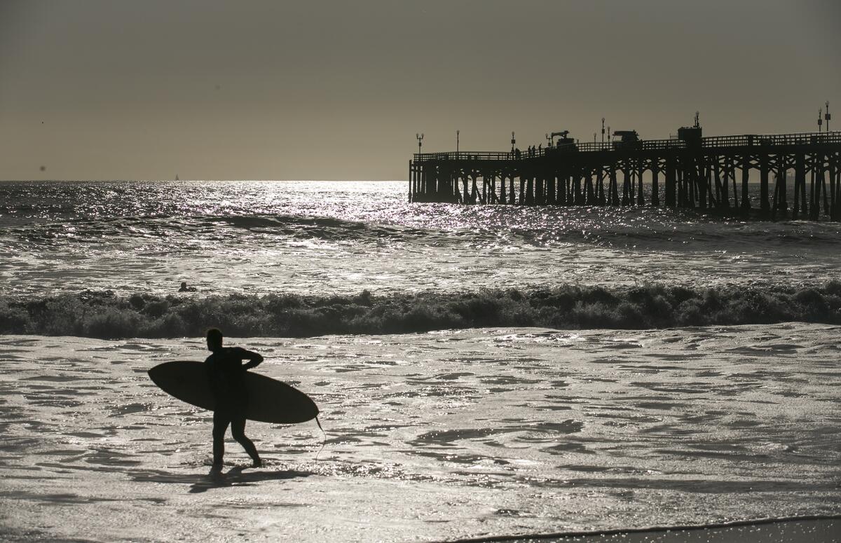 Crews work on the Seal Beach Pier as a surfer enters to water.
