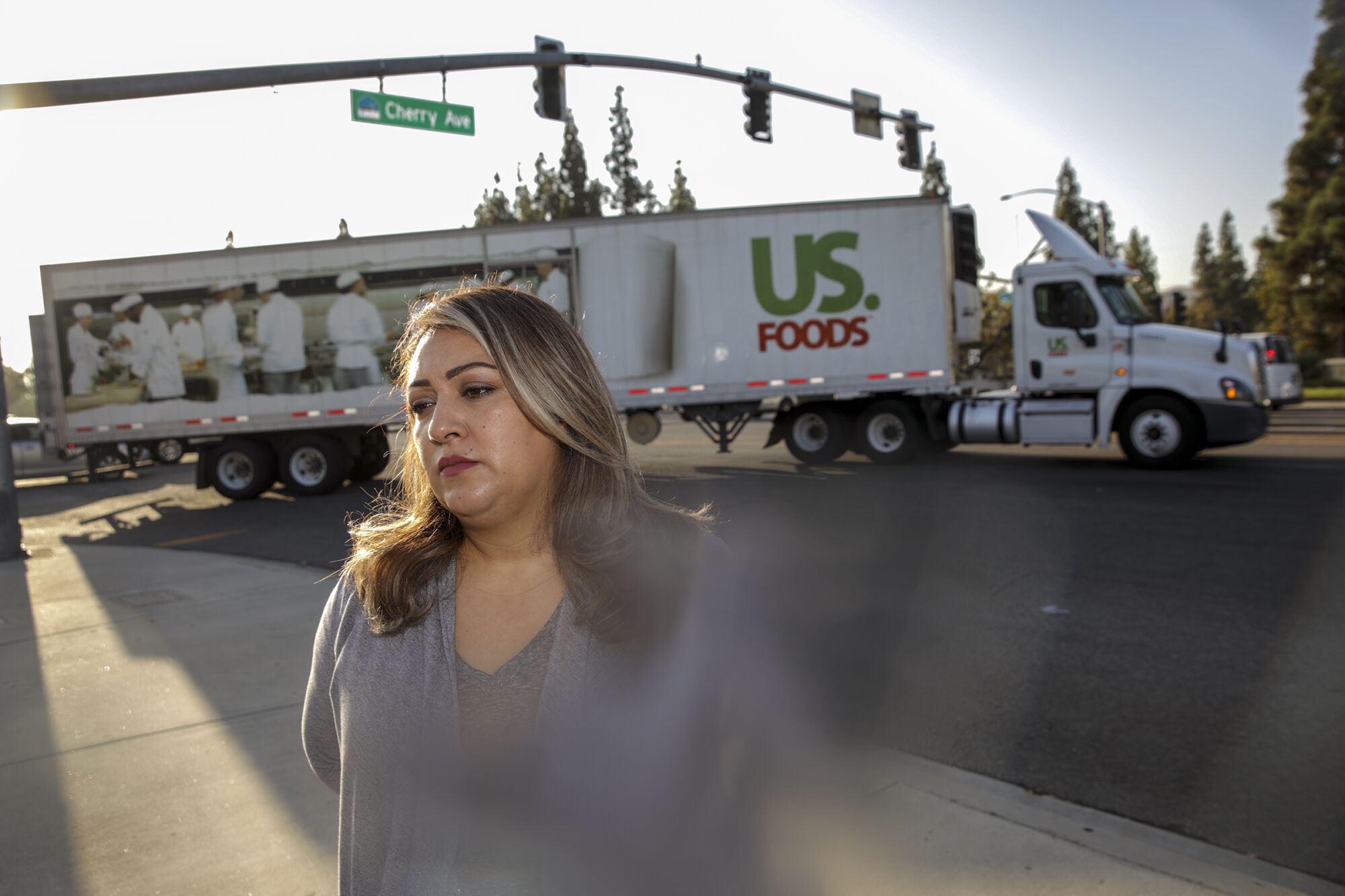 Liz Sena stands on a sidewalk with a large truck behind her