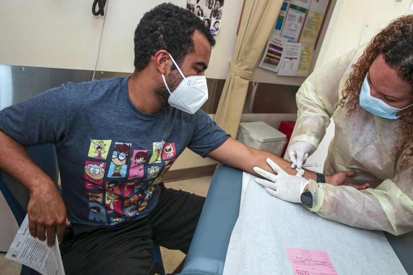 Los Angeles, CA - August 10: A voice actor Isaac Robinson-Smith, 32, left, watches as a medical assistant Elisa Nunez administers a Monkeypox virus vaccine at St.John's Well Child & Family Center on Wednesday, Aug. 10, 2022 in Los Angeles, CA. (Irfan Khan / Los Angeles Times)