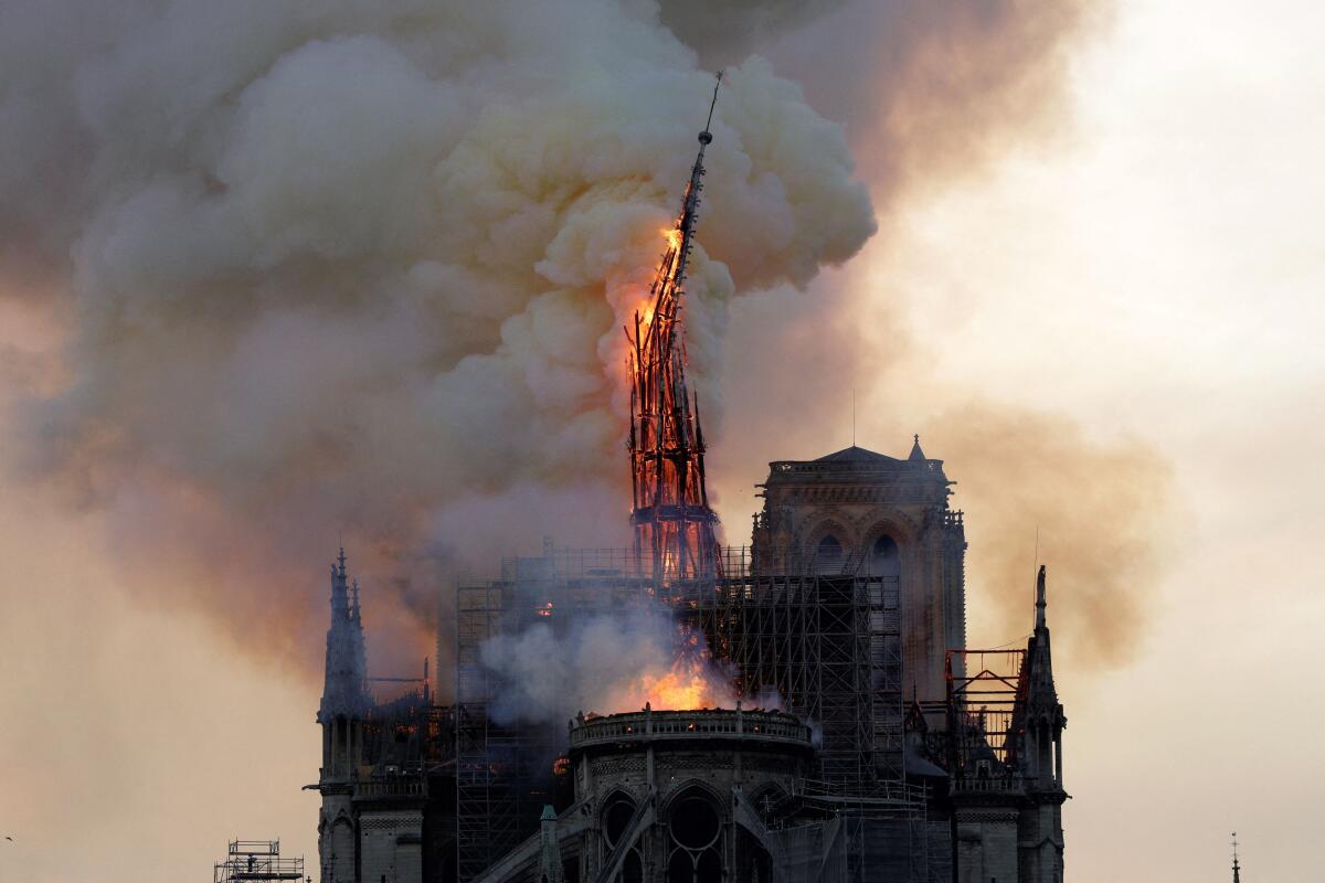 The spire of Notre Dame Cathedral falls, aflame.