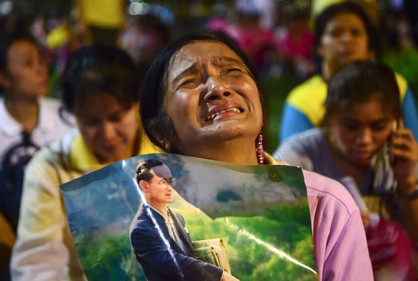 A woman holds a photo of Thailand's King Bhumibol Adulyadej as people react to his death.