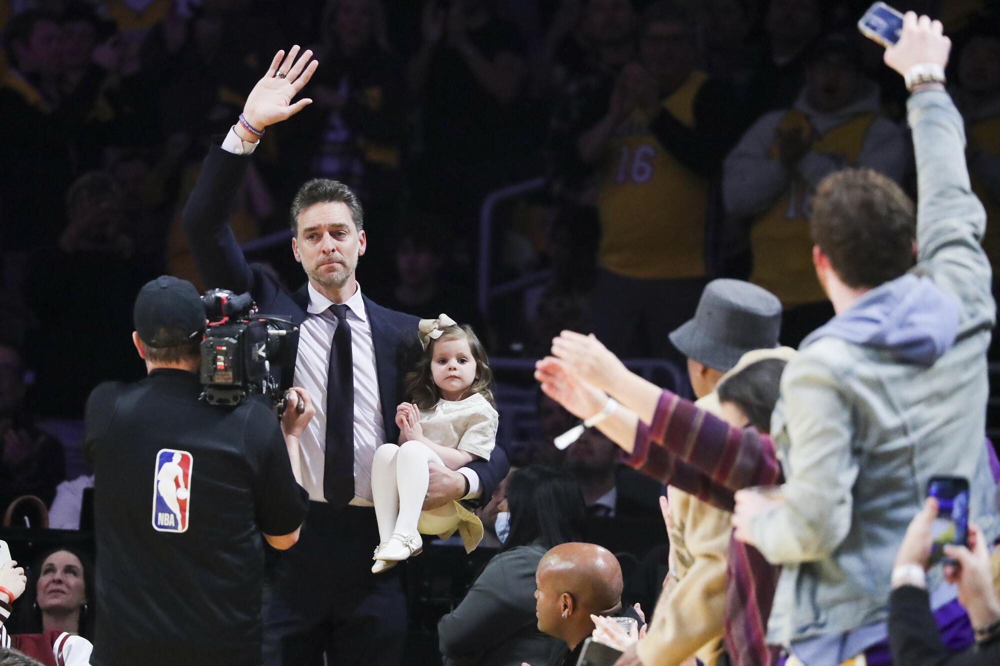 Pau Gasol waves to the fans while holding onto his daughter Elisabet Gianna Gasol as he makes his way on the court.