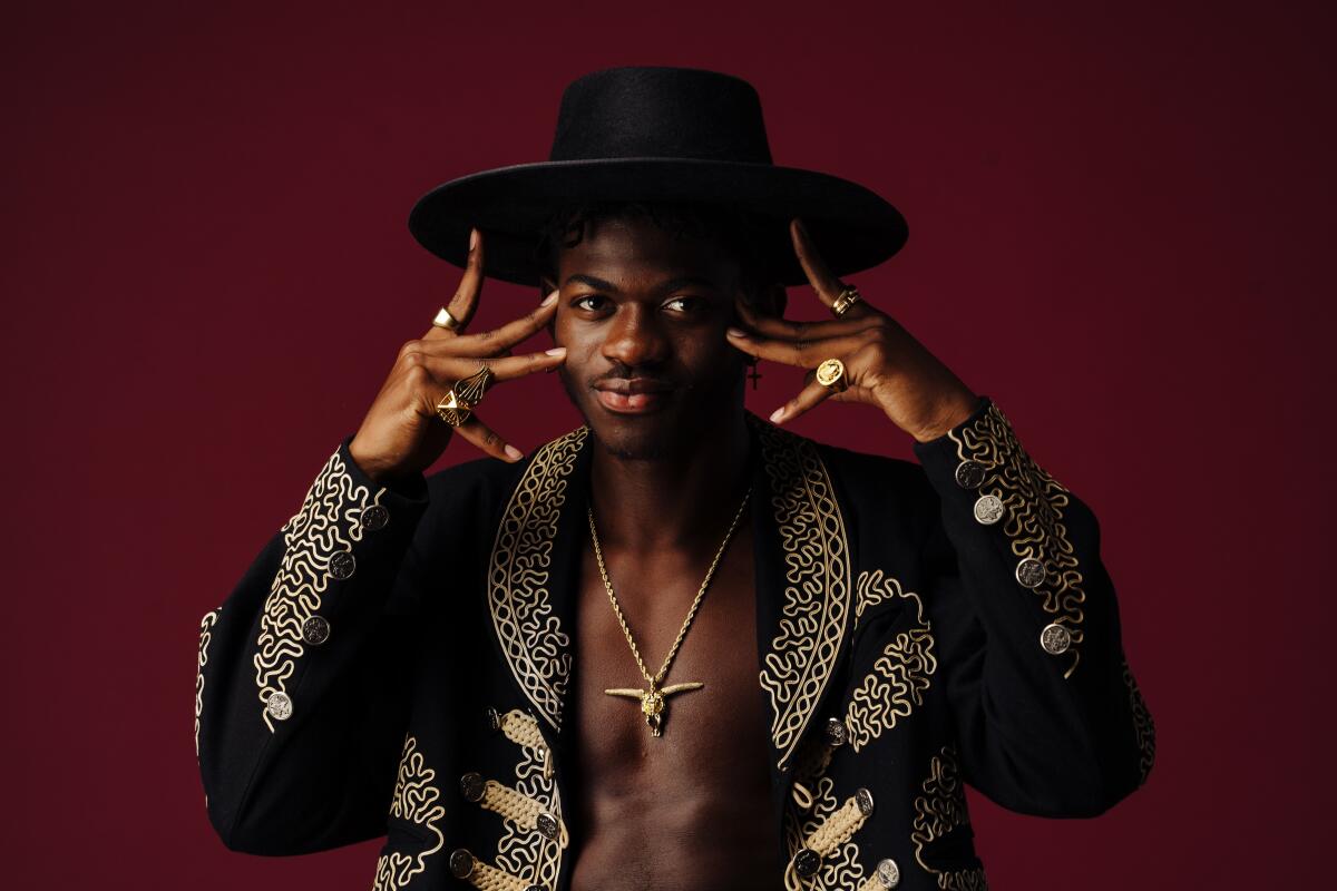 A man posing in a black cowboy hat and gold-trimmed black jacket.