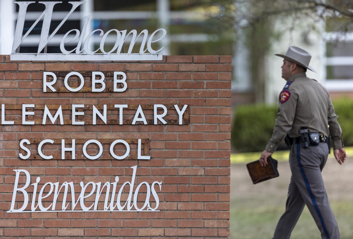 A state trooper walks past the Robb Elementary School sign.