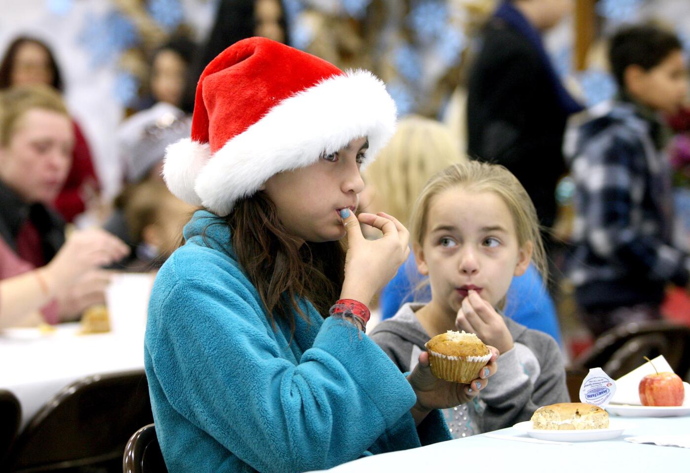 Lexi Arandia, 10 of La Cañada Flintridge, 10, left, and Ashley Fostrey, 9 of Montrose, right, enjoy a muffin and juice before heading out to meet Santa Claus and grabbing a toy or two at the Crescenta Valley Sheriff Station's annual Toy and Food Drive at Crescenta Valley Park in La Crescenta on Saturday, Dec. 19, 2015.