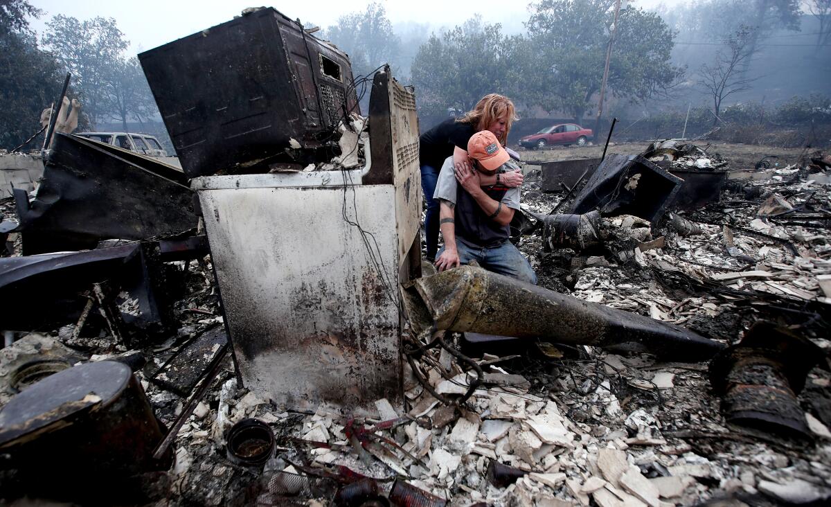 Two people embrace in the charred remains of their home.