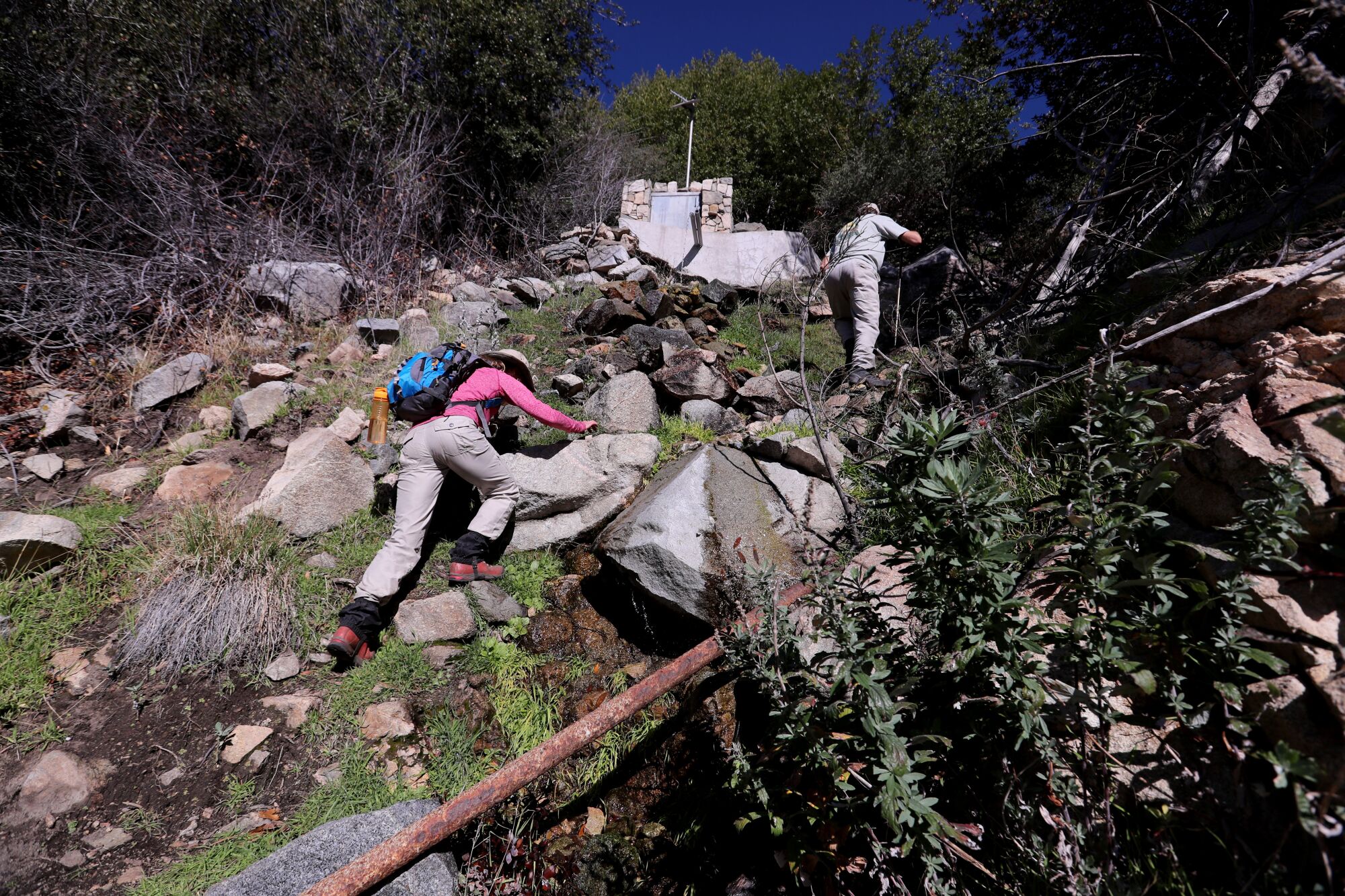 People hike up a slope where water trickles down.