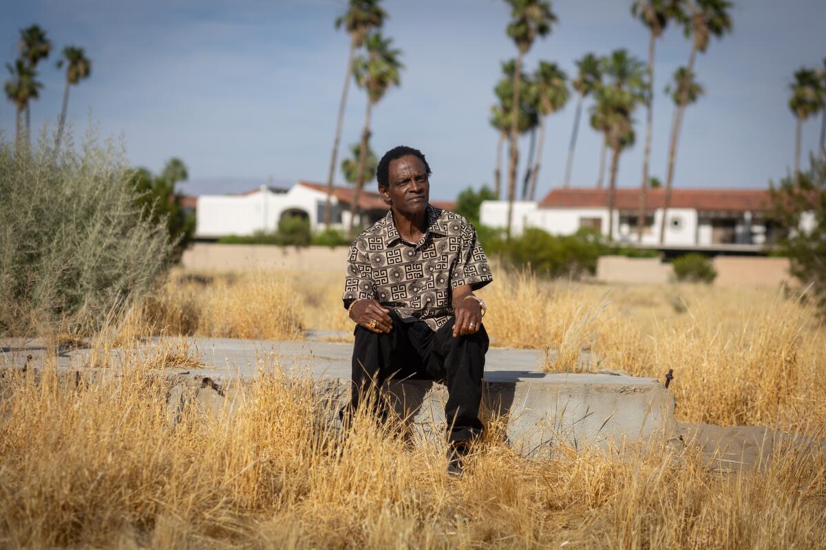 A man sits on a slab of concrete in a field filled with weeds.