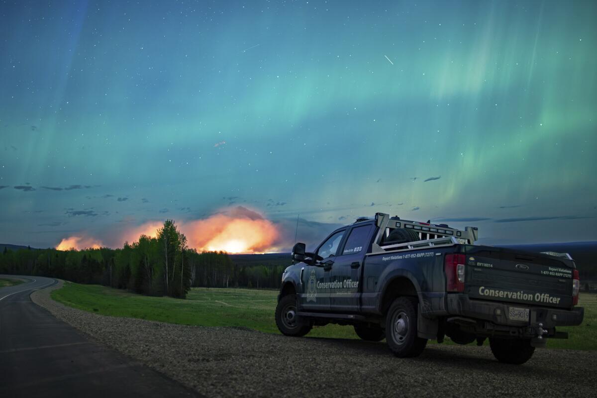 A wildfire burns in the distance with northern lights overhead.