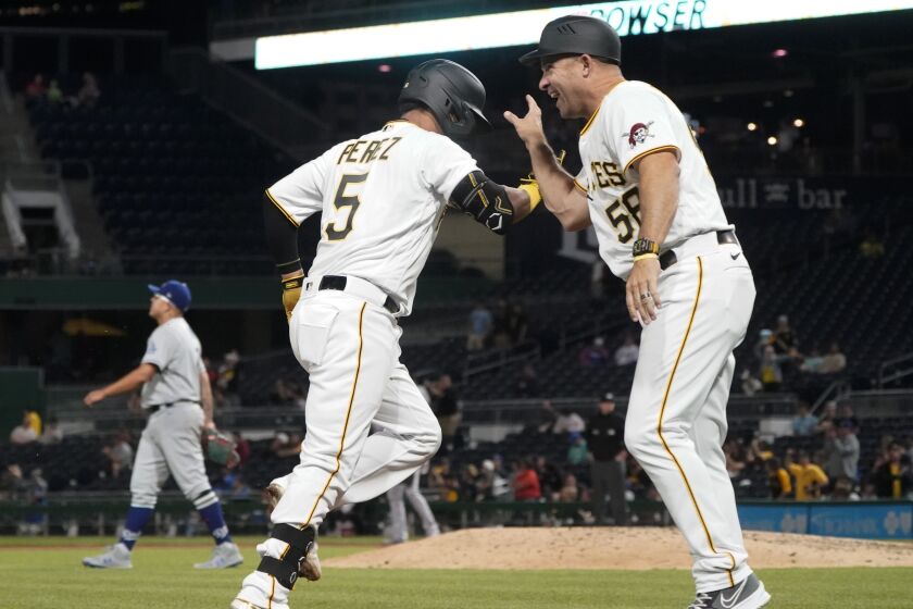 Pittsburgh Pirates third base coach Mike Rabelo, right, greets Michael Perez (5) who rounds the bases after hitting a solo home run off Los Angeles Dodgers starting pitcher Julio Urias, back left, during the seventh inning of a baseball game, Monday, May 9, 2022, in Pittsburgh. (AP Photo/Keith Srakocic)