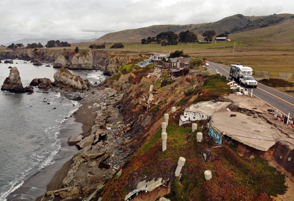 Crumbled concrete and seawalls on an eroding bluff between the ocean and a two-lane highway