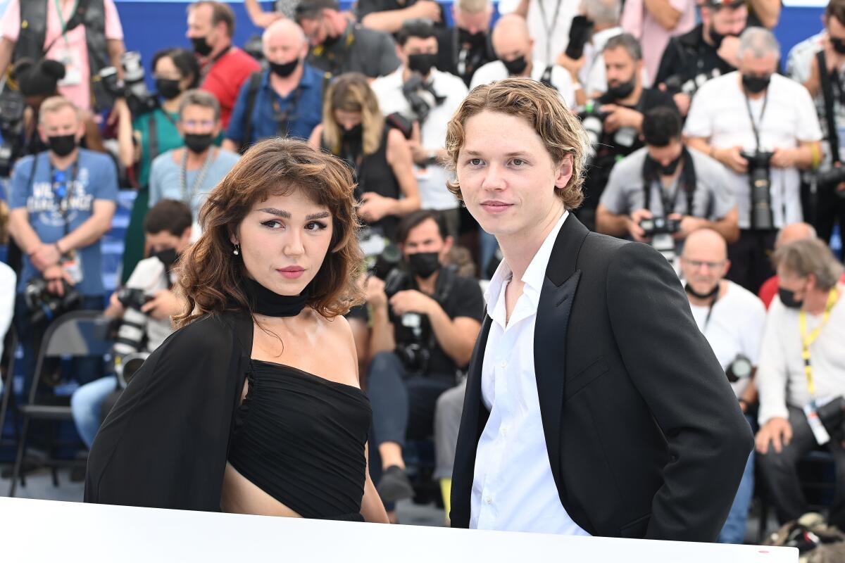 A young woman and a young man pose in front of a crowd of people.