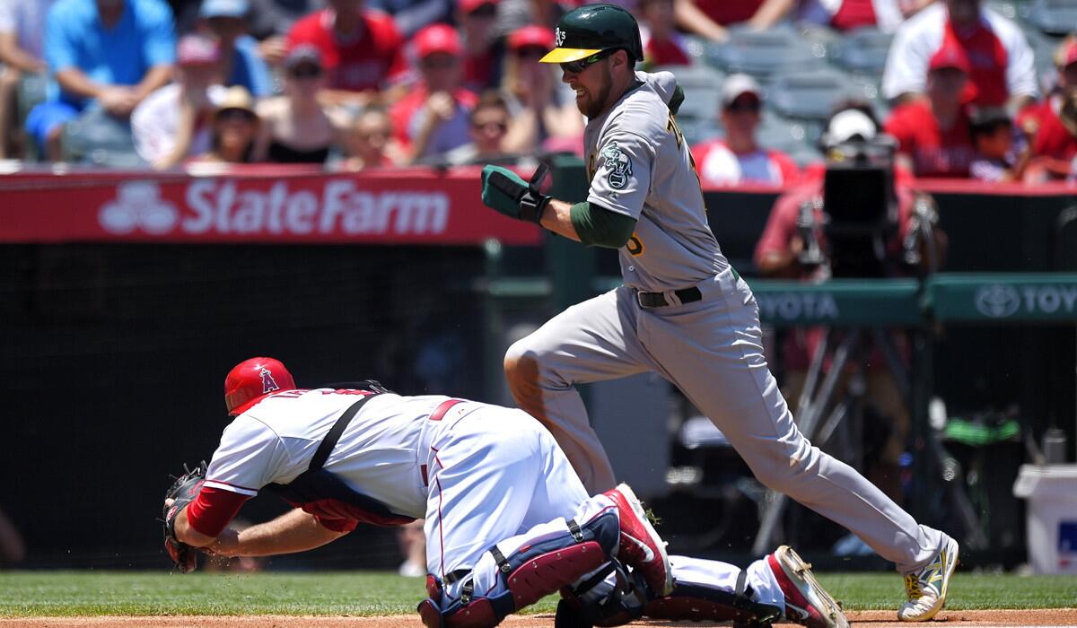 Oakland Athletics' Ben Zobrist gets ready to jump over Los Angeles Angels catcher Chris Iannetta as he scores on a ball hit by Eric Sogard during the second inning on Sunday. Iannetta was charged with an error on the play.
