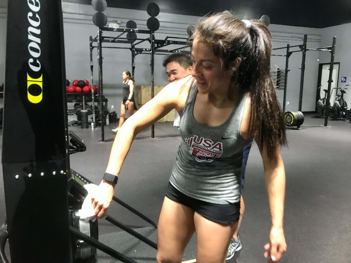 Natalia Guzman, of OC Fit in Tustin, wipes down equipment with disinfectant wipes.