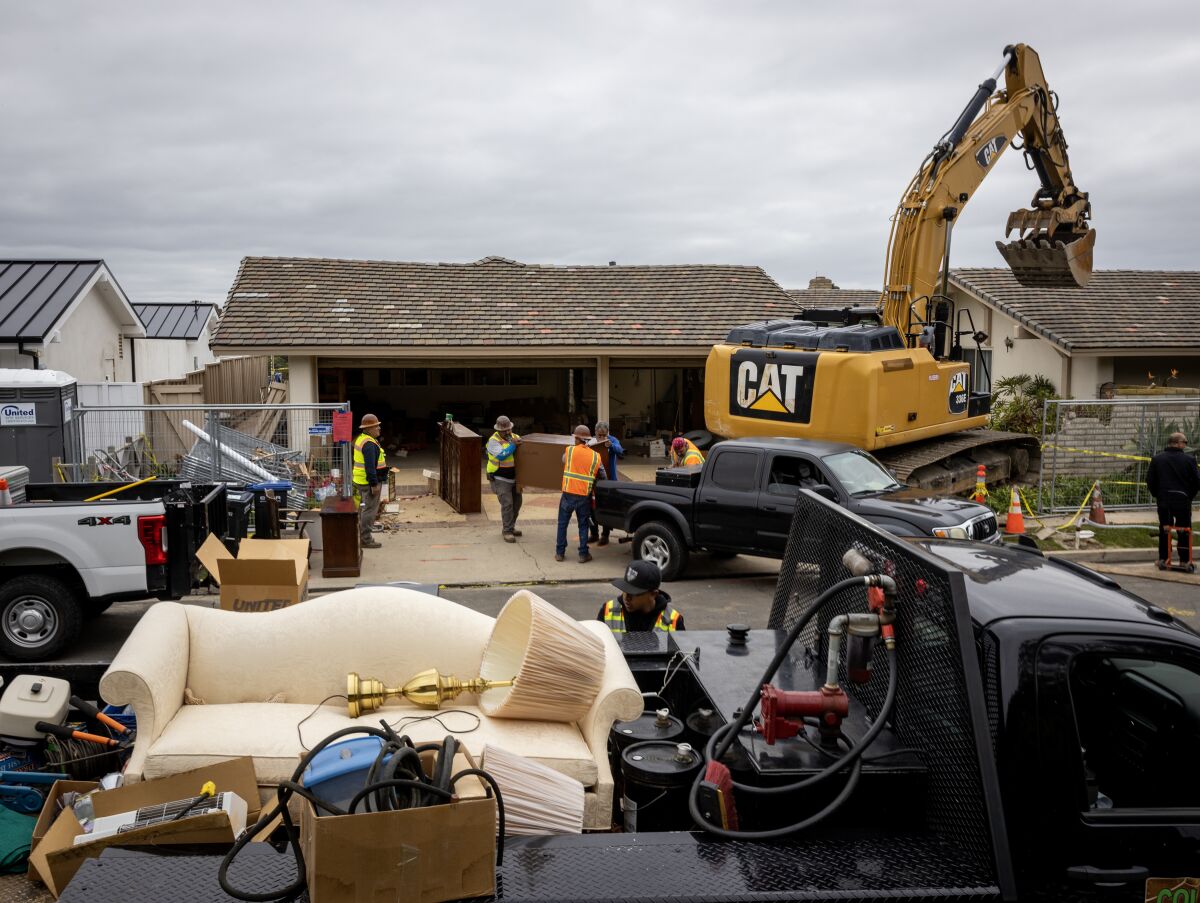A couch, lamps and boxes of belongings are in a truck parked in front of a house near a bulldozer.