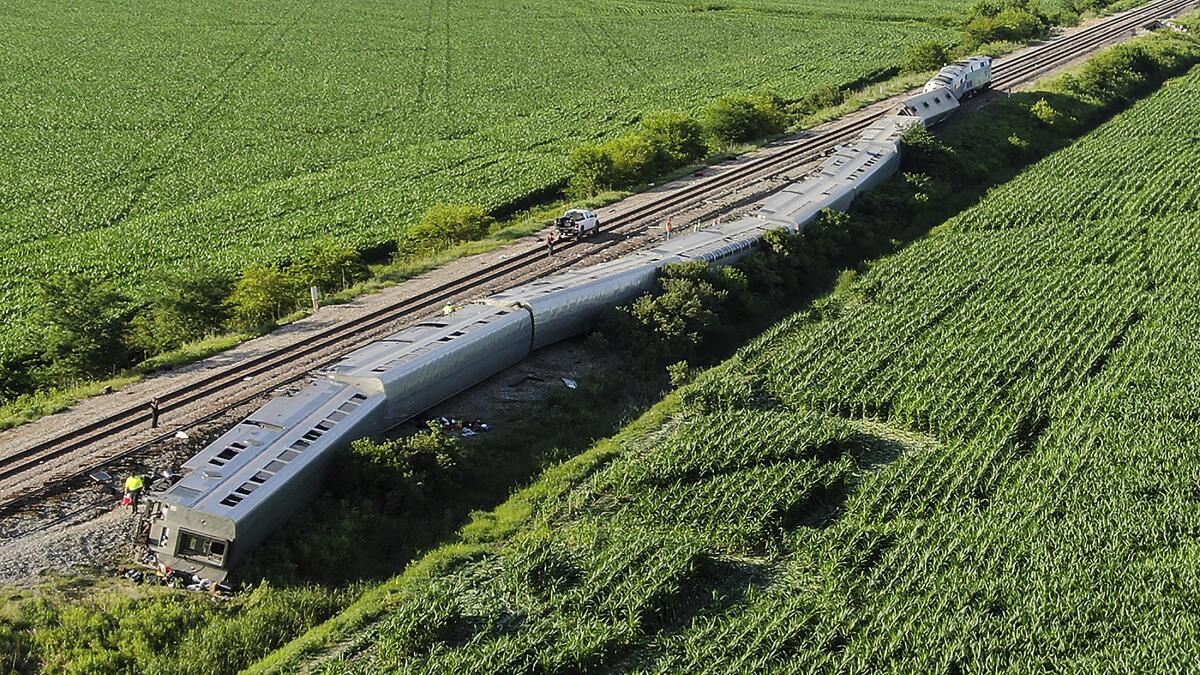 Several train cars lie on their side next to railroad tracks between fields