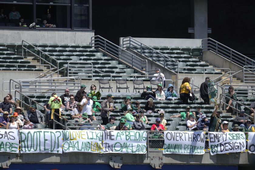 Fans watch from behind signs hanging in right field during the fifth inning of a baseball game between the Oakland Athletics and the Houston Astros in Oakland, Calif., Saturday, May 27, 2023. (AP Photo/Jeff Chiu)