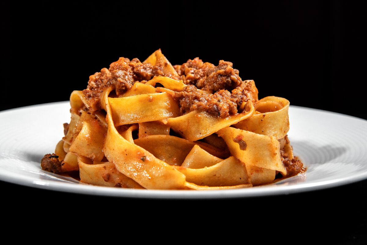 A plate of wide pasta with meat sauce on top 