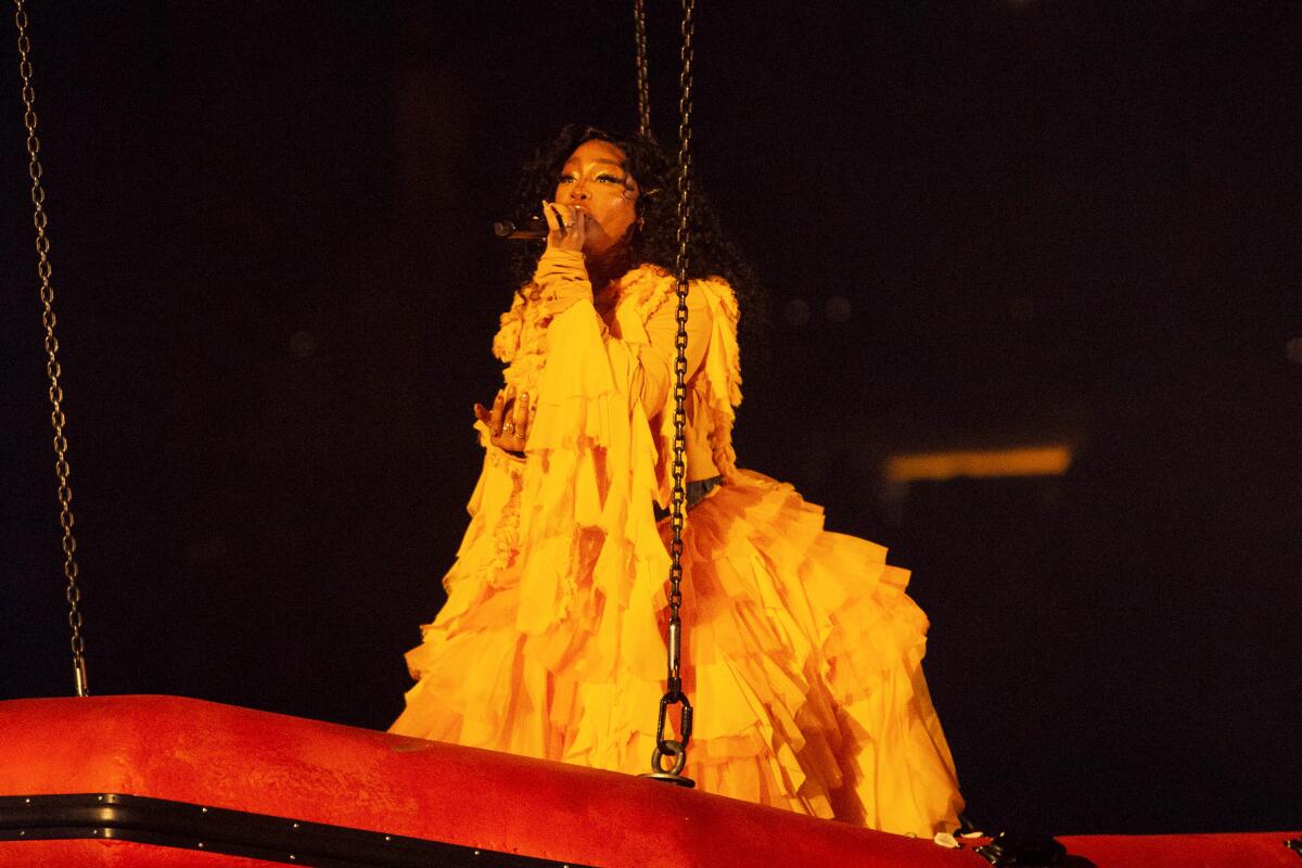 A female singer in a yellow dress performs in concert suspended on a platform