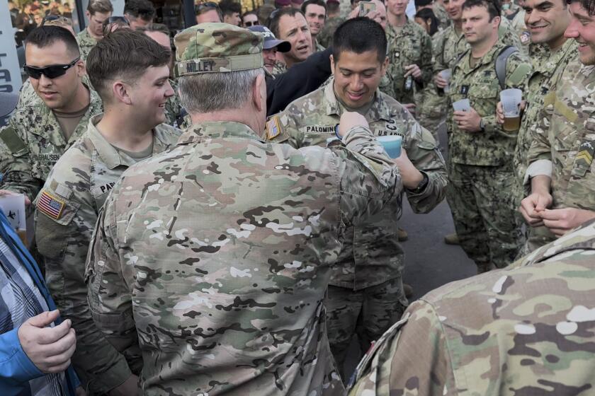 Joint Chiefs Chairman Gen. Mark Milley drops his chairman's coin into Capt. Palomino's beer as he walks through crowds of soldiers celebrating the anniversary of D-Day in the town square of Sainte-Mere-Eglise in Normandy, France on June 4, 2023. This was Milley's last visit to Normandy as a soldier, just a few months before he was to retire, and he soaked it in talking to soldiers and veterans, and handing out his chairman's coin to many of them. (AP Photo/Tara Copp)