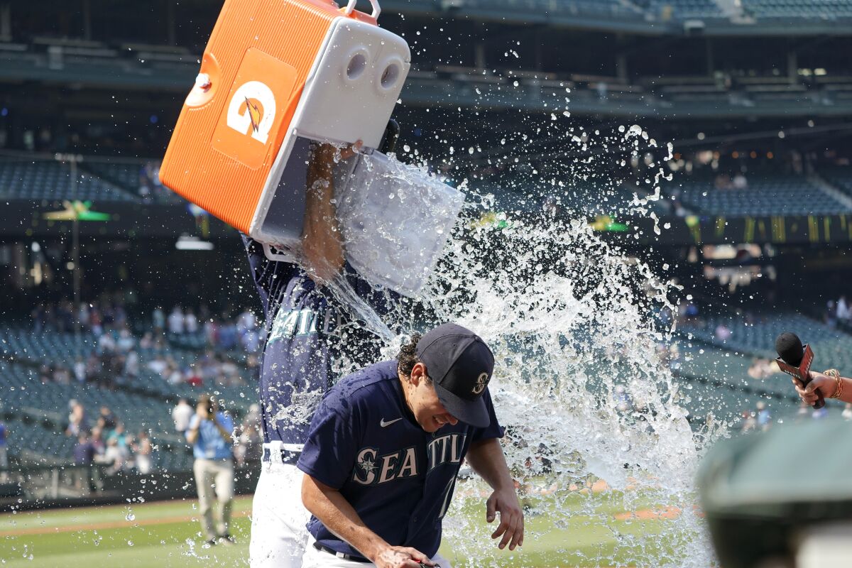 Seattle Mariners starting pitcher Marco Gonzales is doused with water by catcher Tom Murphy while taking part in a TV interview after the team's baseball game against the Texas Rangers, Thursday, Aug. 12, 2021, in Seattle. Gonzales threw a two-hitter as the Mariners won 3-1. (AP Photo/Ted S. Warren)