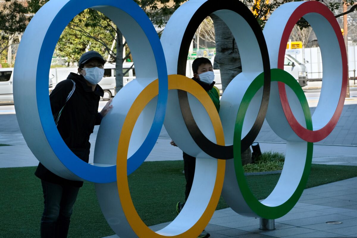 Two people pose at an installation of the Olympic rings in Tokyo on Tuesday. The IOC, Japanese Prime Minister Shinzo Abe and local organizers decided to postpone the Tokyo Games because of the coronavirus.