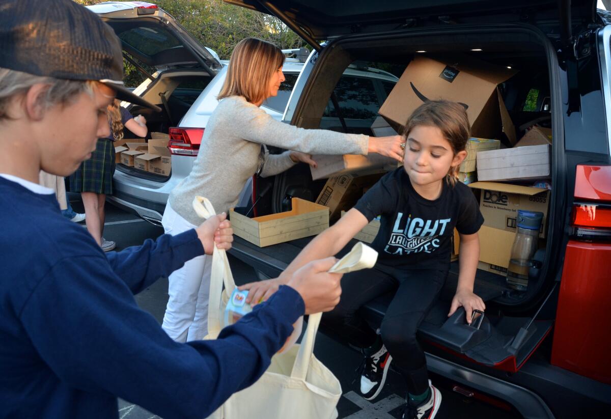 Skye Krout, 7, places a box of fruit cups into a volunteer's bag during Trunk & Pack food drive.