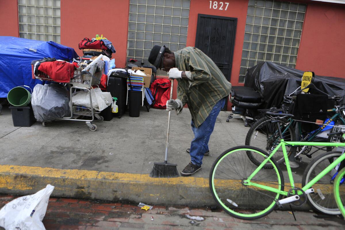 Roy Carter, a 57-year-old homeless man, sweeps the sidewalk where his belongings are gathered on South Hope Street in January. Over the last two years, hundreds of street encampments have jumped their historic borders in downtown Los Angeles, lining the 110 Freeway and filling underpasses from Echo Park to South Los Angeles.
