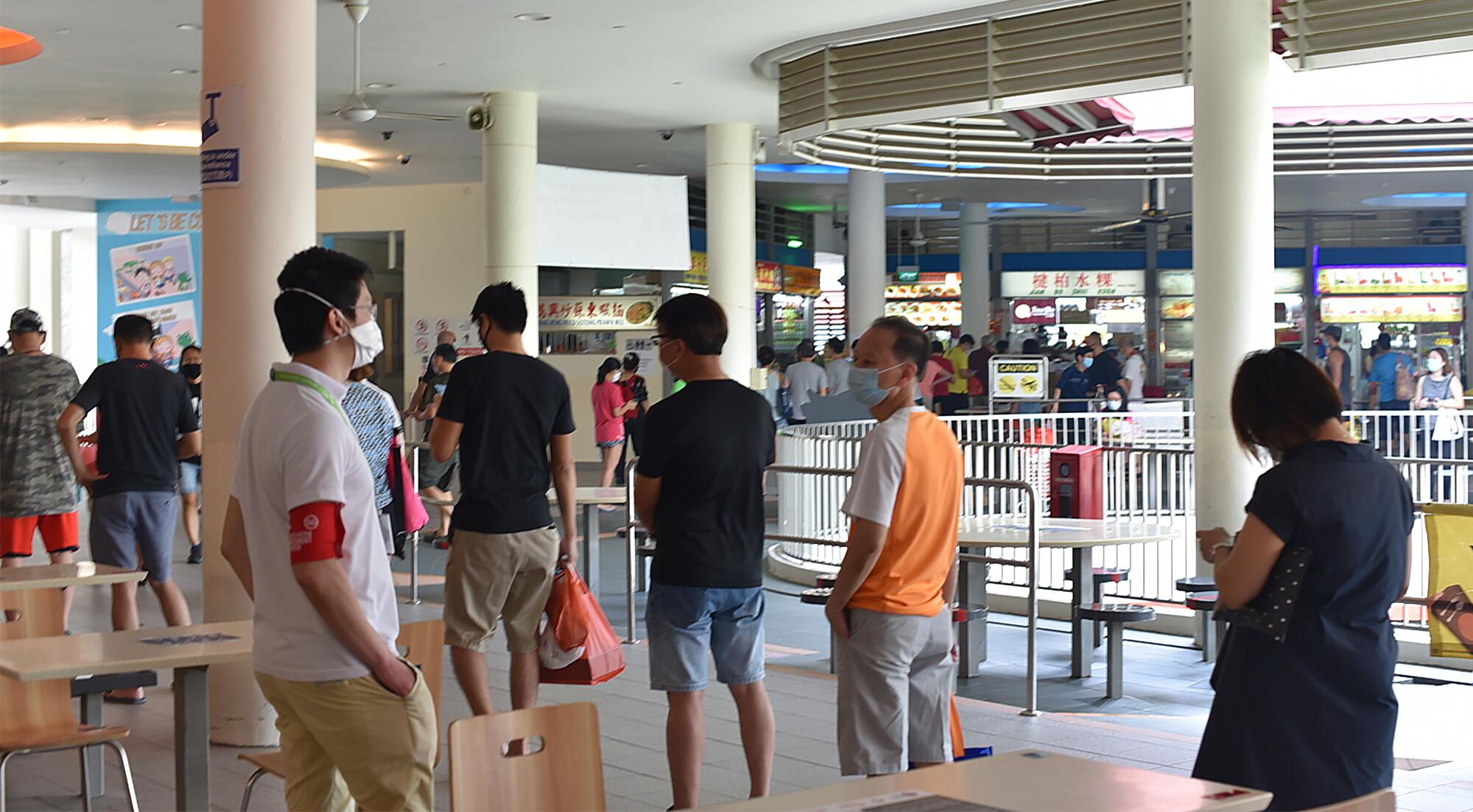 A so-called safe-distancing ambassador wearing a red armband watches over customers lining up at a food court in Singapore on April 18.