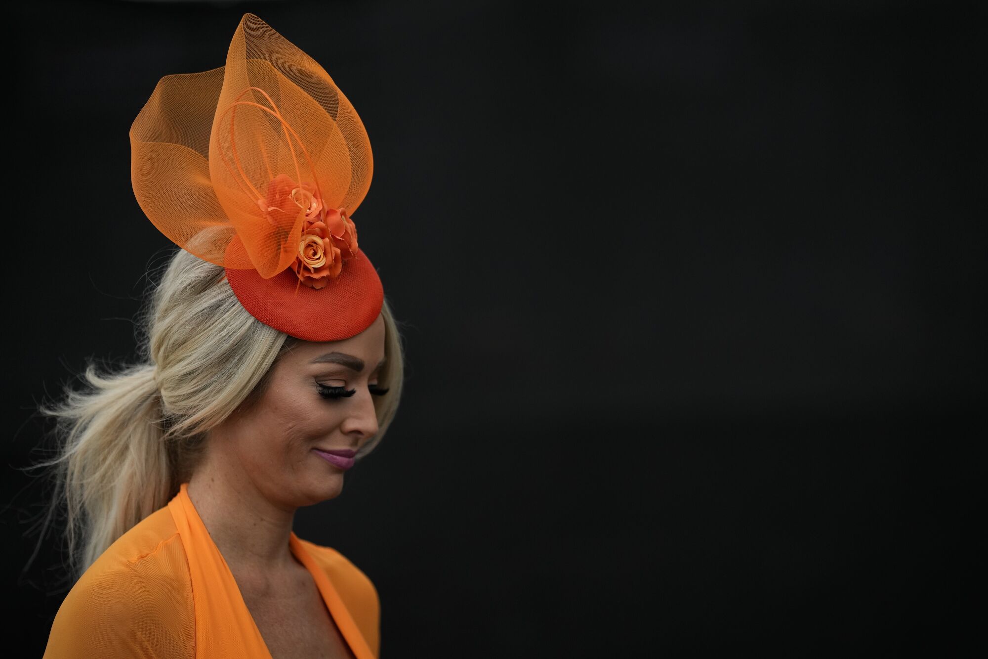 A woman wearing a tall orange hat walks to her seat at Churchill Downs 