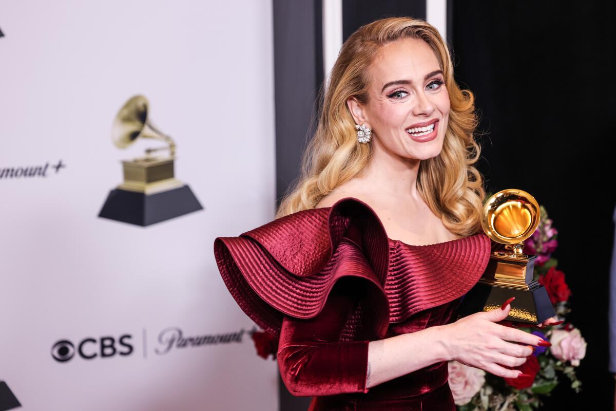 Adele smiles while wearing a ruffle-shouldered dress and holding a Grammy Award