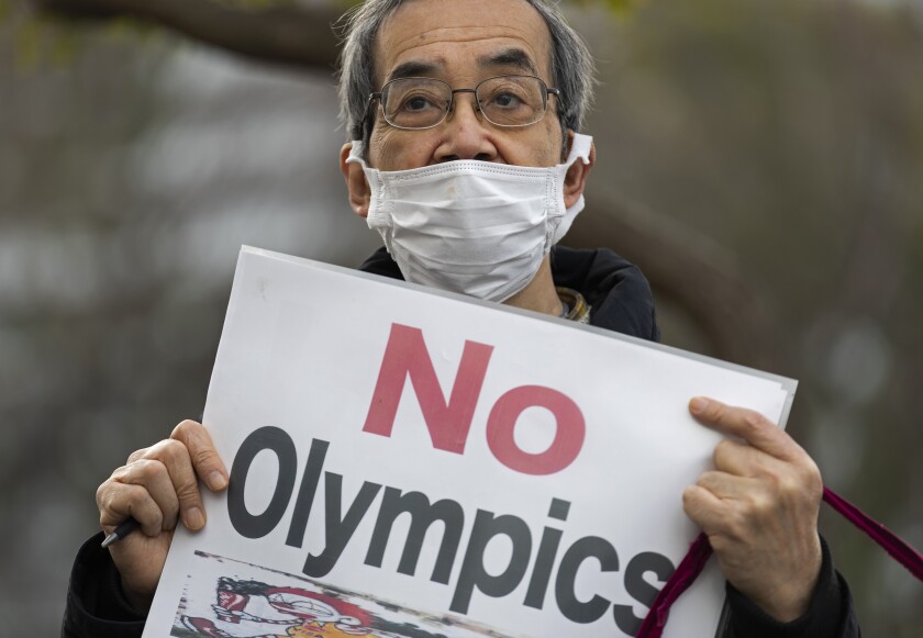 A demonstrator holds a placard protesting the planned Tokyo 2020 Olympic games near a building where Yoshiro Mori was meeting to announce his resignation as the president of the Tokyo Olympic organizing committee in Tokyo on Friday, Feb. 12, 2021. Mori resigned Friday, following sexist comments implying women talk too much. (AP Photo/Hiro Komae)