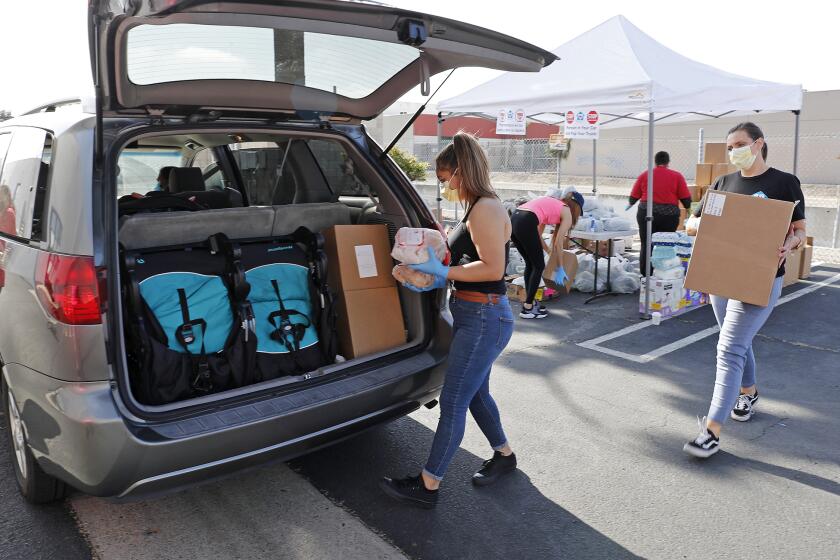 Volunteer Silvia Gomez, center, and case manager Lacy Morek, right, load food into the trunk of a minivan during a drive-thru food distribution at Colette's Children's Home on Saturday morning. The Huntington Beach-based nonprofit organization provides housing and supportive services to homeless women and children throughout Orange County.