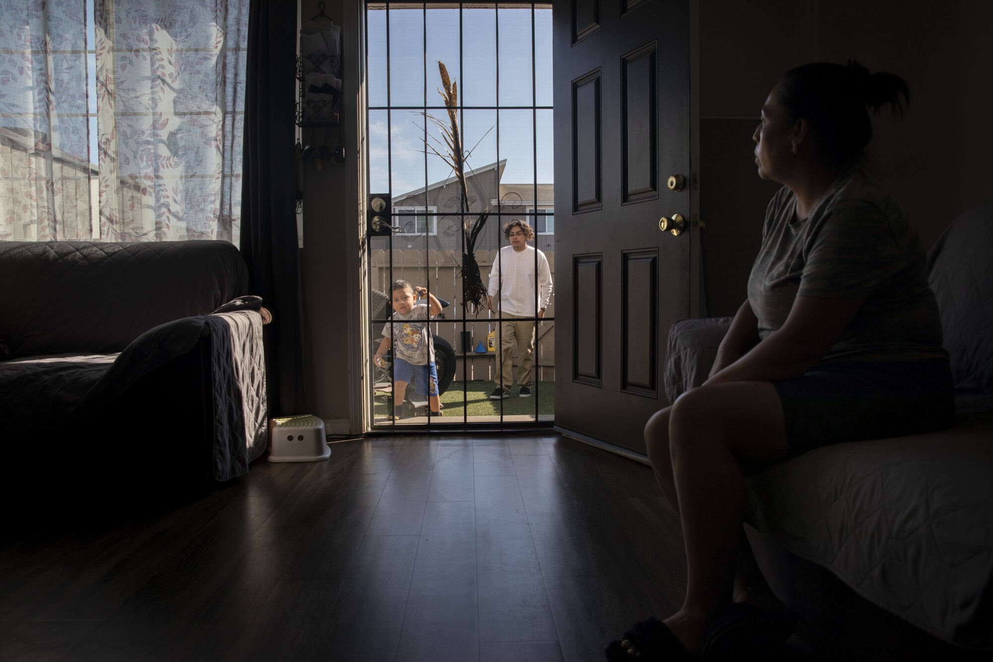 A woman in a living room with the door open to the outside, with a baby and a man outside the door  