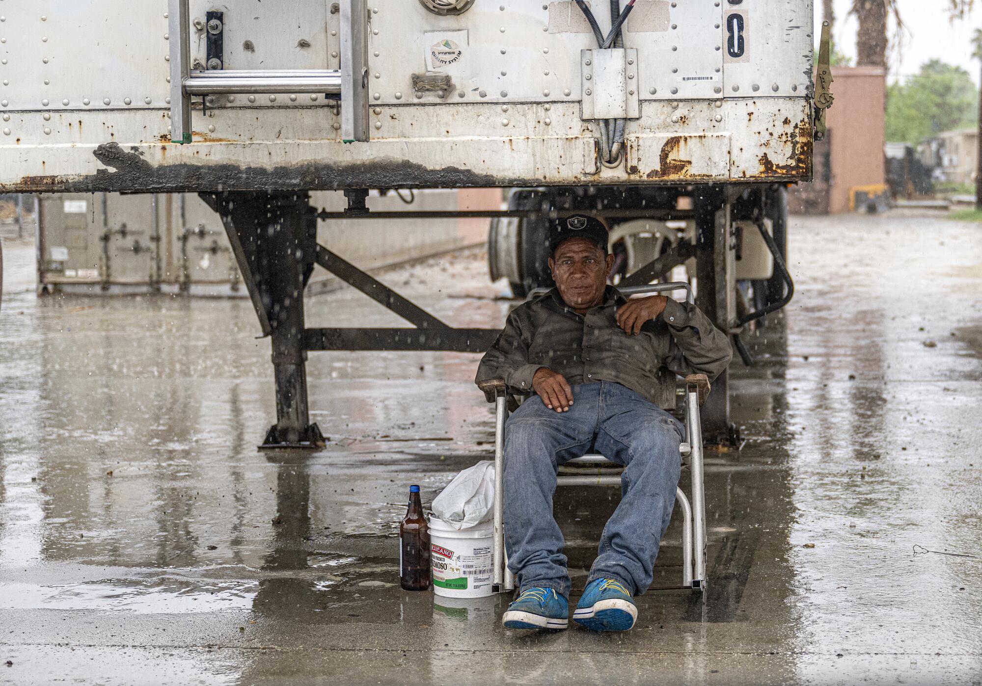 A man sits in a chair under a white big rig while it rains