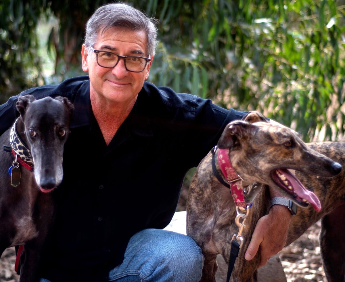 A man with his arms around dogs on either side of him 