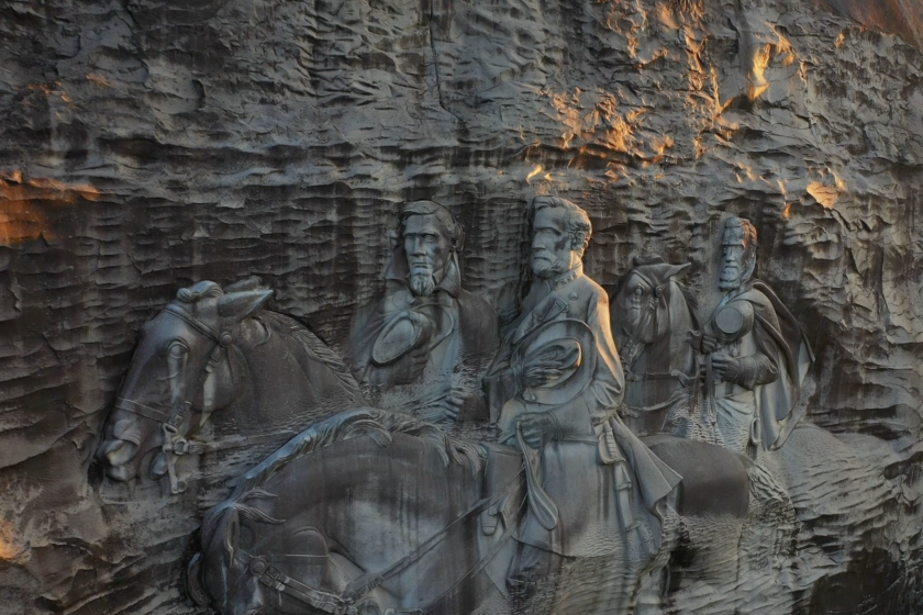 A drone's eye view of a towering rock facade bears bas relief carving of Confederate leaders on horseback