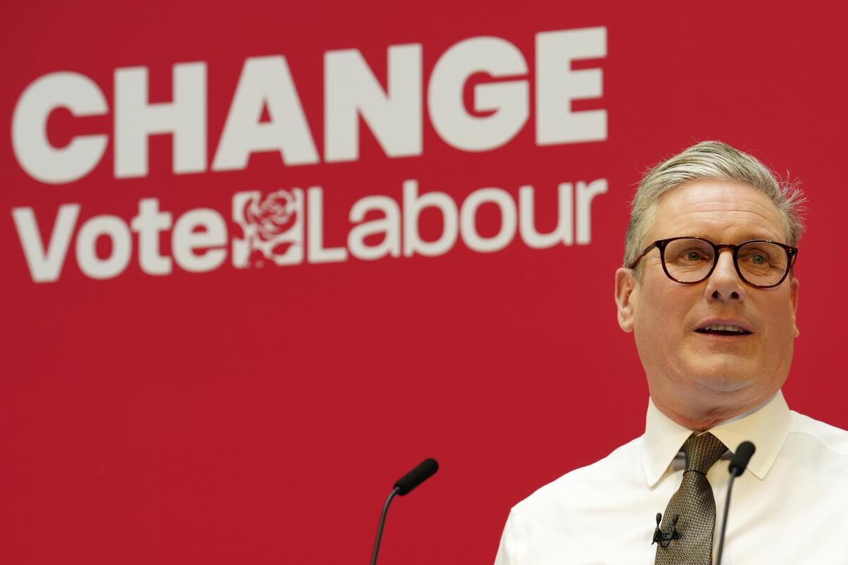 A man in glasses speaks into a microphone in front of a red backdrop with words in white: "Change: Vote Labour."
