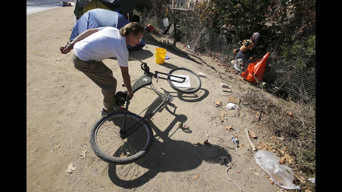 Larry Ford, a homeless veteran, picks up his Army bike next to his shelter at a homeless encampment along the Santa Ana River trail in Fountain Valley.