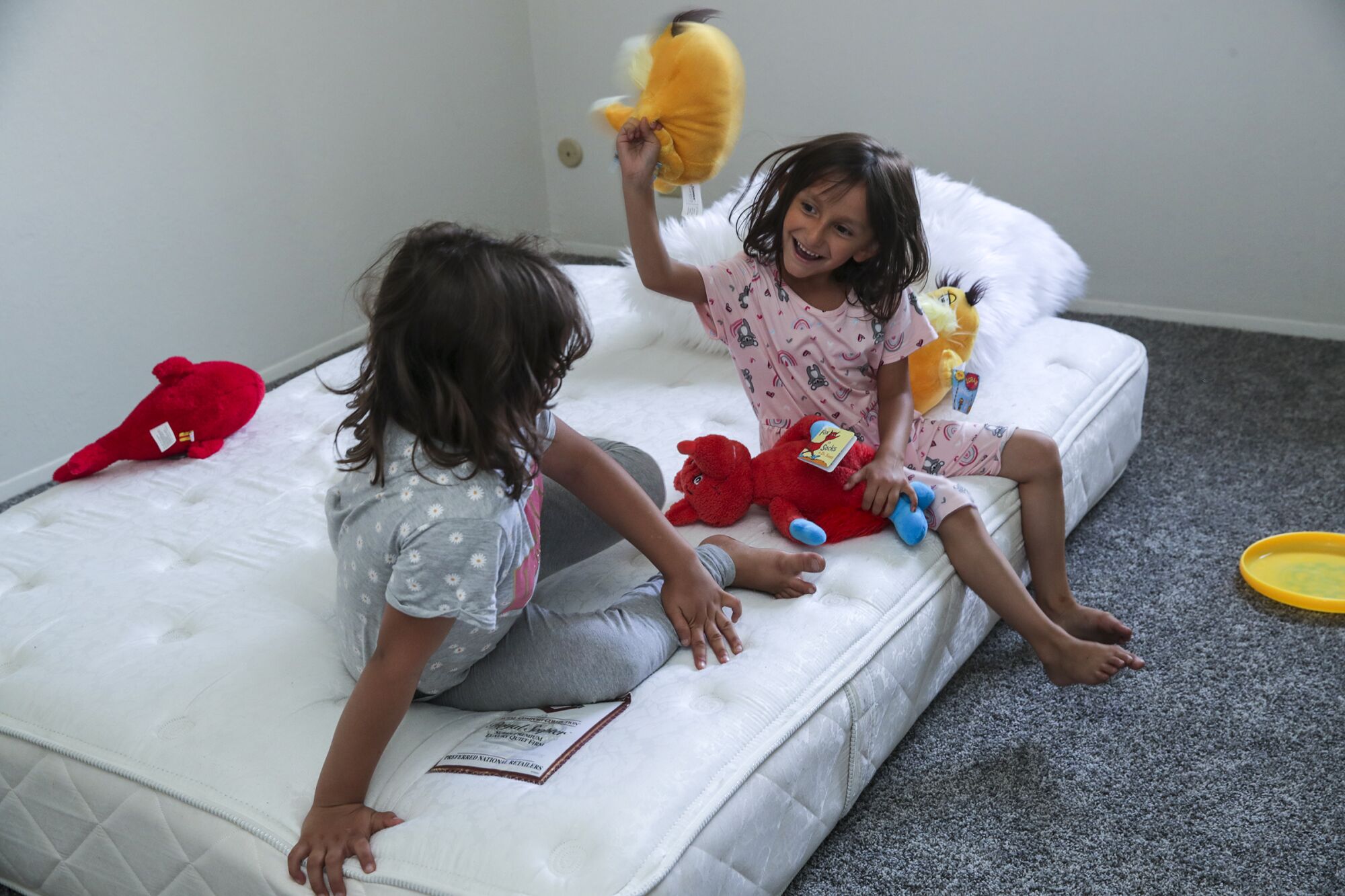 Afghan refugees Gulsom Sadat, 9, left, and her sister, Aqsa Sadat, 6, play on a mattress in their apartment in El Cajon.